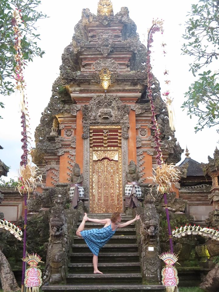 Photo of Carly Hopper stretching her leg while practicing yoga on the steps of an ornate Asian style monastery.
