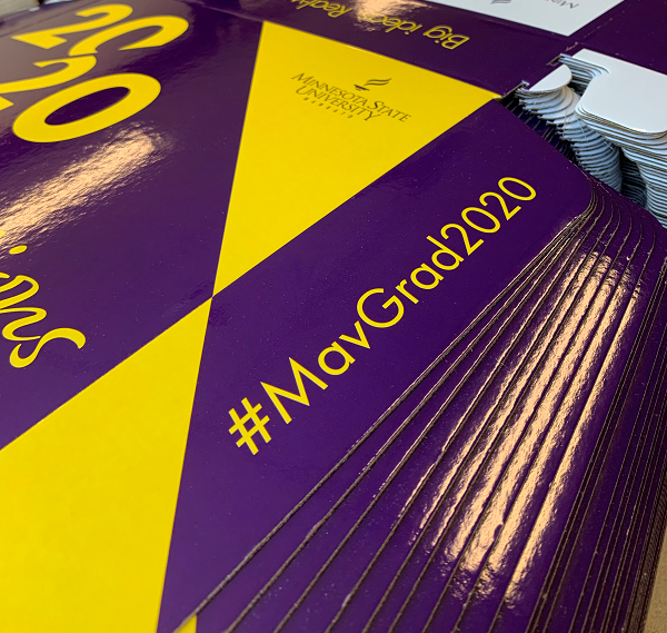 Stacks of printed purple and gold branded boxes used for commencement-in-a-box mailings