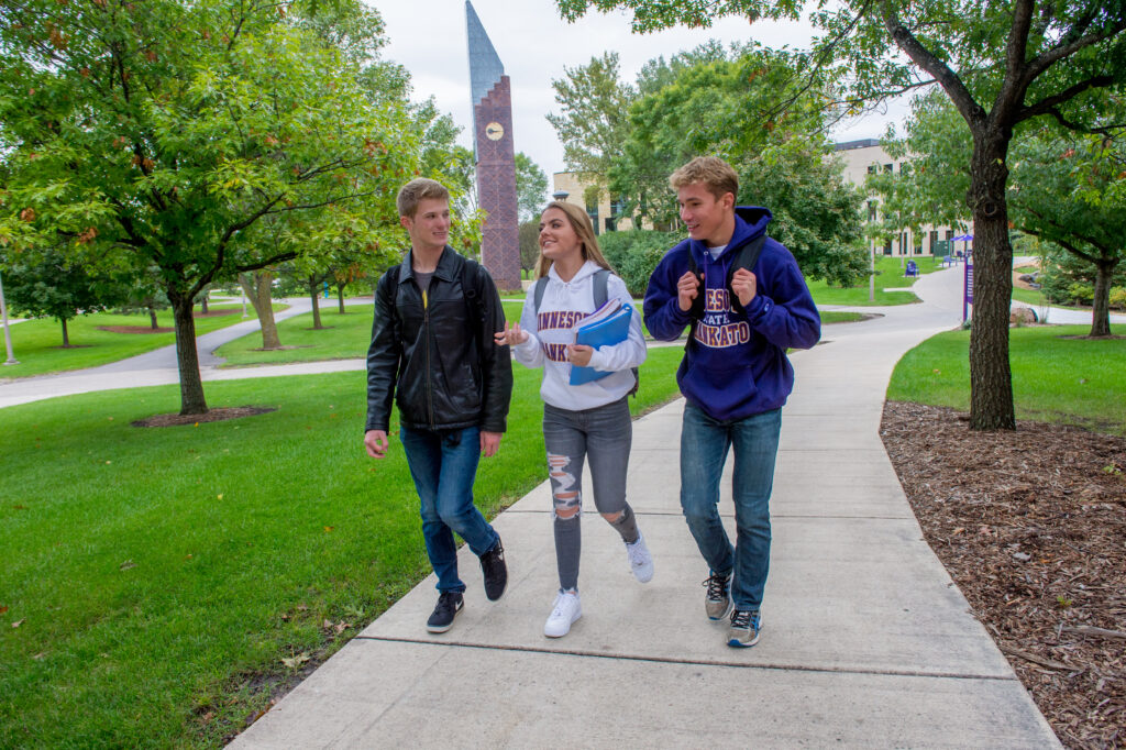 three students walking past the iconic bell tower at Minnesota State University Mankato